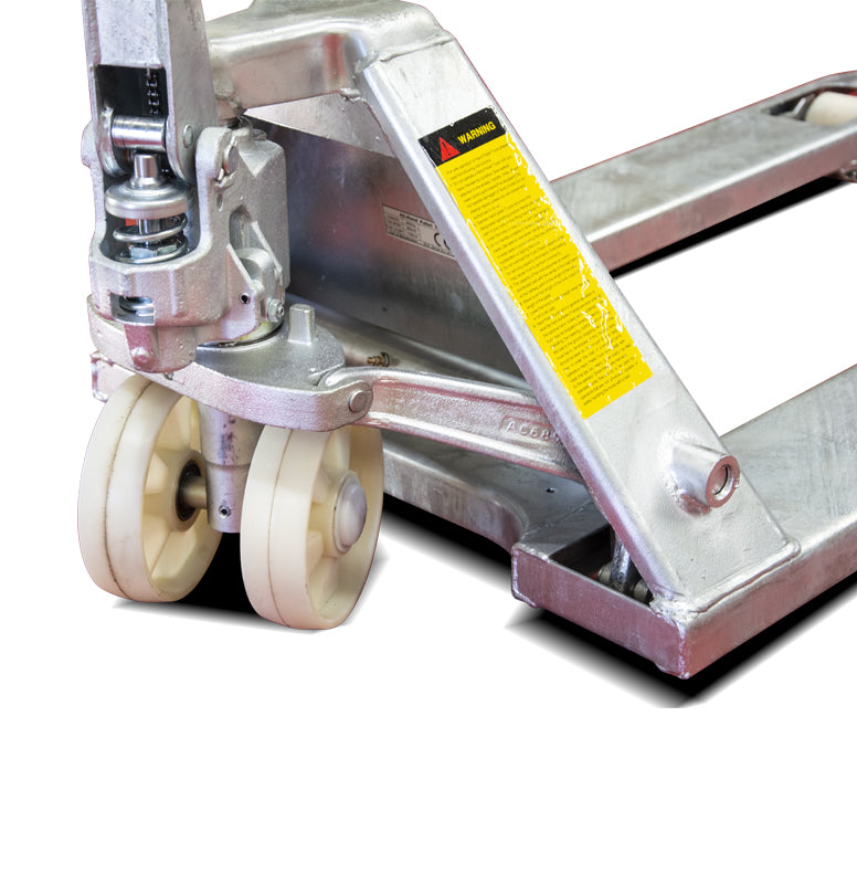 Close-up of a hydraulic pallet jack with silver metal body and yellow warning label; two sturdy white rubber wheels visible.