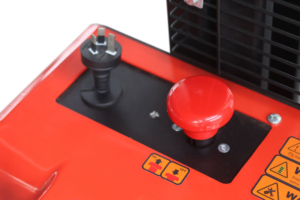 Top view of a red machine control panel featuring an emergency stop button, power socket, and safety warning labels.