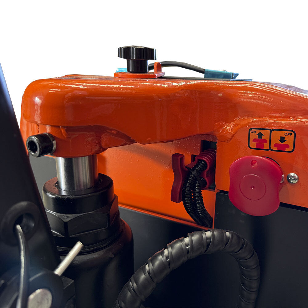 Close-up of a power pallet jack with an orange body, control knobs, a red emergency stop button, and visible hydraulic components.