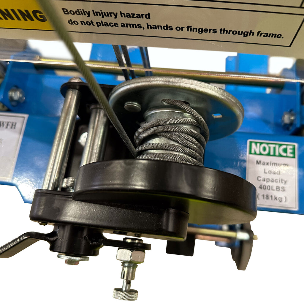Close-up of a pulley system with a warning label about bodily injury, showcasing metal cable and components on a blue machine.